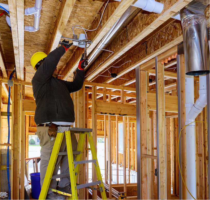 Electrician in a hard hat wiring electrical conduit inside a commercial building under construction